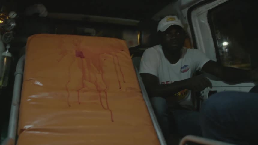 A man is sitting next to a bloody ambulance bed