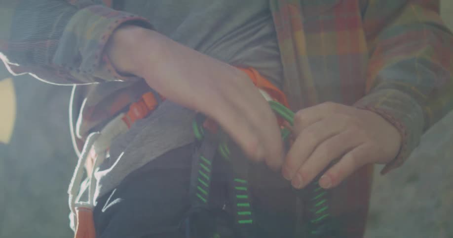 A persons hands as they meticulously fasten and adjust their harness and other climbing gear preparing for a climb