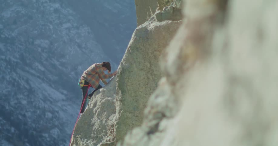Climber secured by rope ascending a steep rock wall