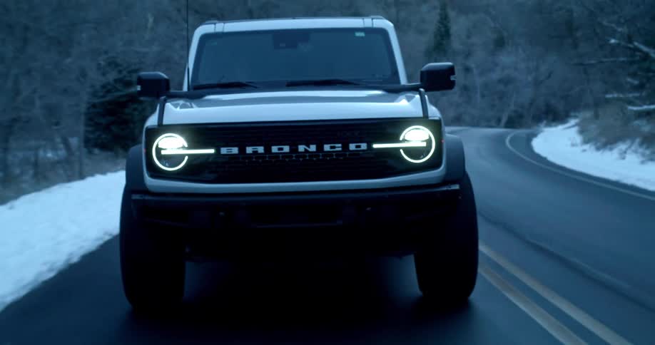 An suv car driving on an asphalt road surrounded by snow and turning on its headlights
