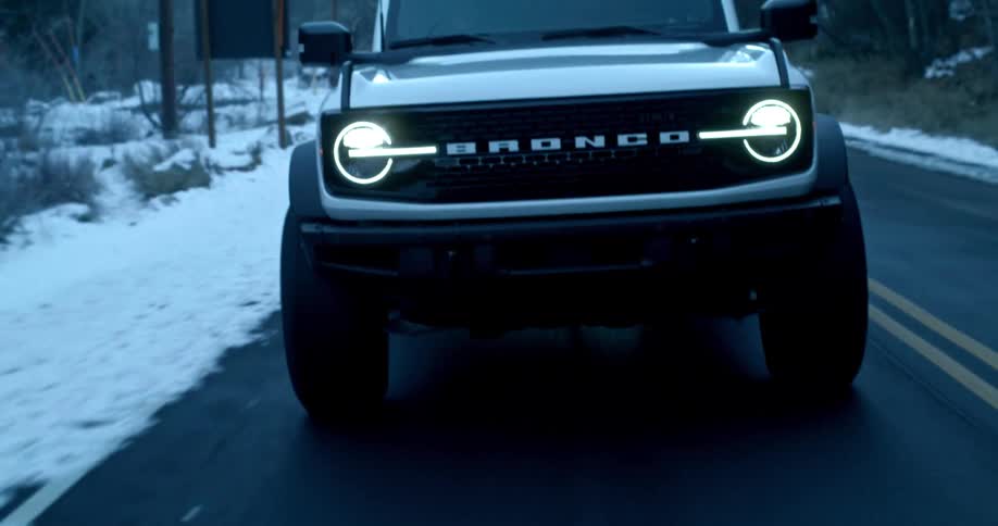 White ford bronco driving on a road with snow on the sides
