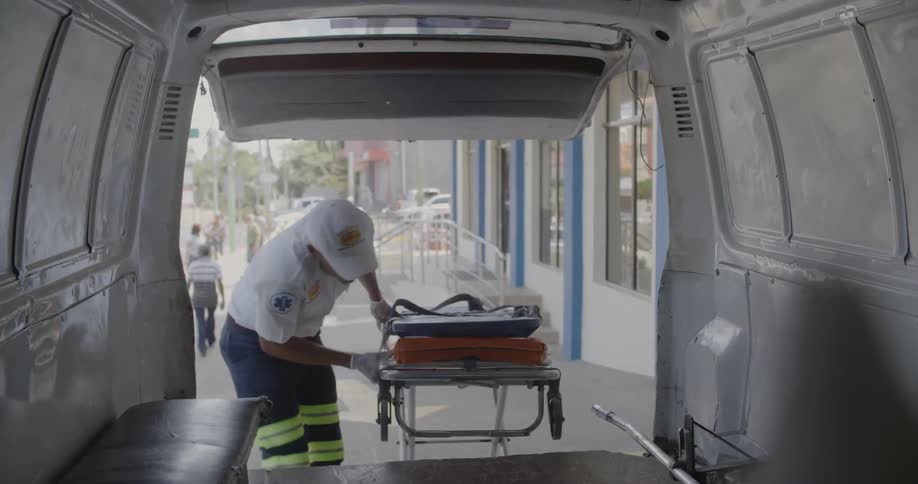 A man wheels are gurney up to the back of an ambulance