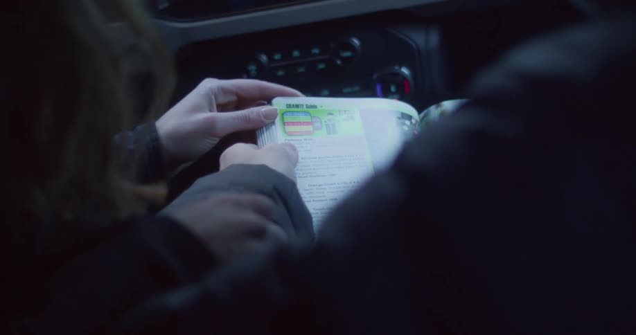 A person is sitting in the passenger seat of a car and looking at a map or brochure the dashboard of the car is visible in the background which appears to be a ford bronco