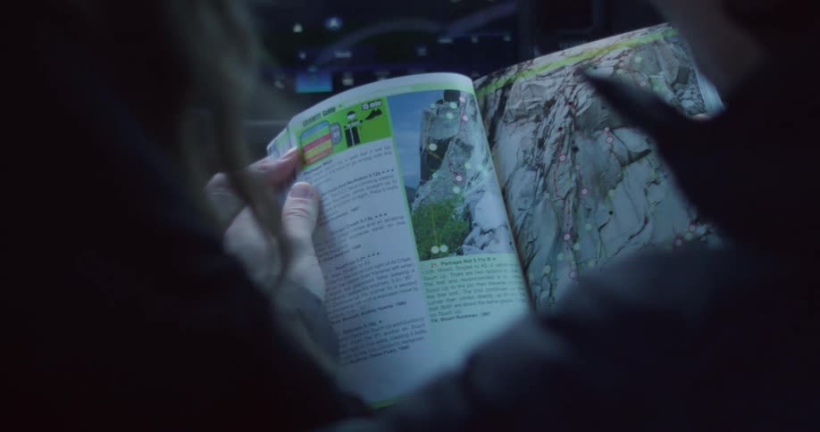 A person points to a page in a book while sitting in a dimly lit vehicle