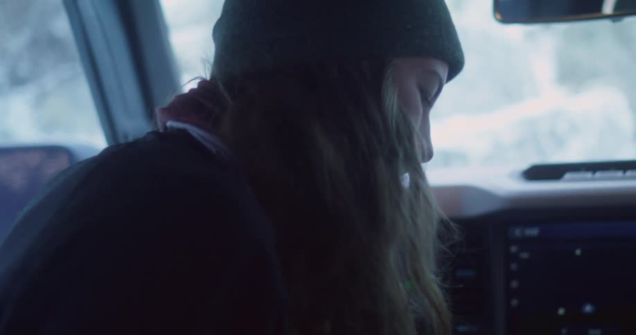 The video shows a person wearing a beanie and a winter coat sitting inside a vehicle the windows are frosty suggesting a cold snowy setting