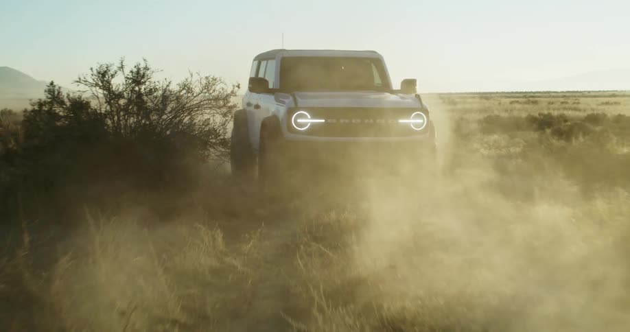 A white bronco suv drives through a dusty grassland on a windy day