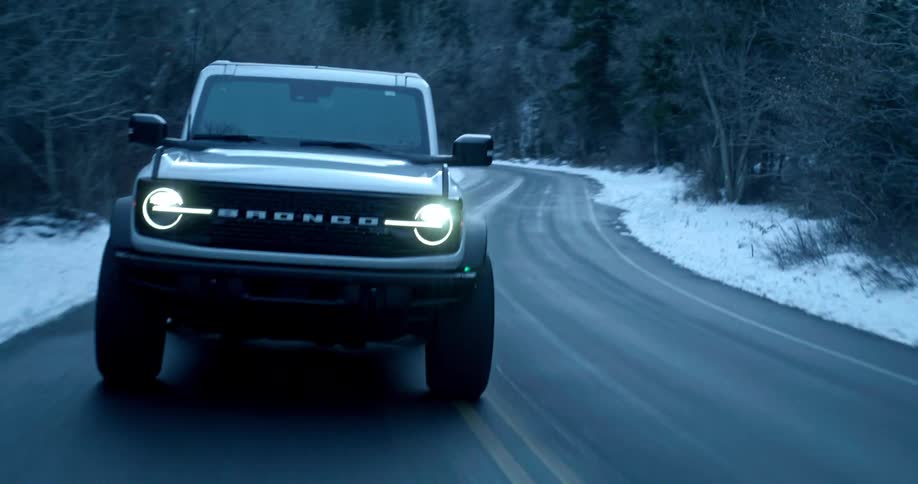 A white jeep driving on an asphalt road with a yellow line in the center and snow on the sides