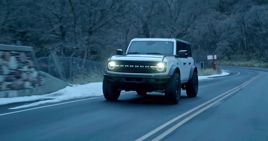 A white jeep driving on an asphalt road in a rural area with vegetation and snow on the sides