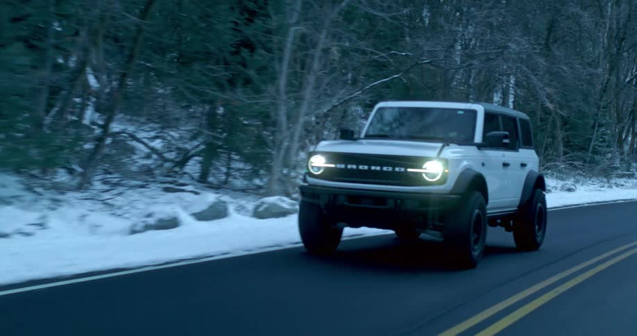 White suv driving on a road surrounded by trees and snow