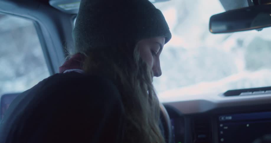 A woman wearing a beanie is talking while seated in a vehicle