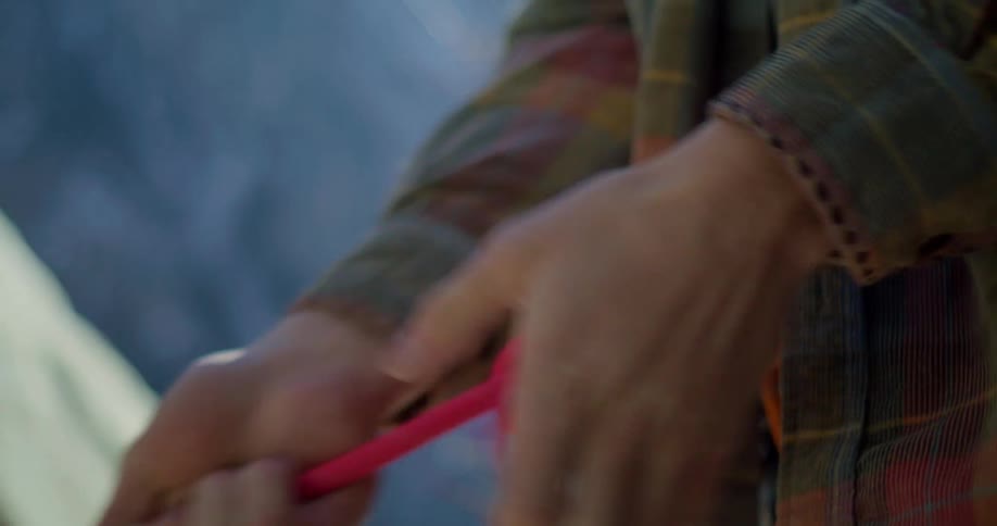 A person in a plaid shirt ties a bright red climbing rope into a knot with both hands