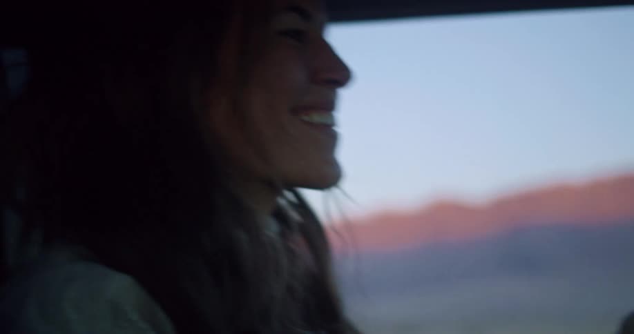 A woman drives happily with a view of sunlit mountains outside the car window