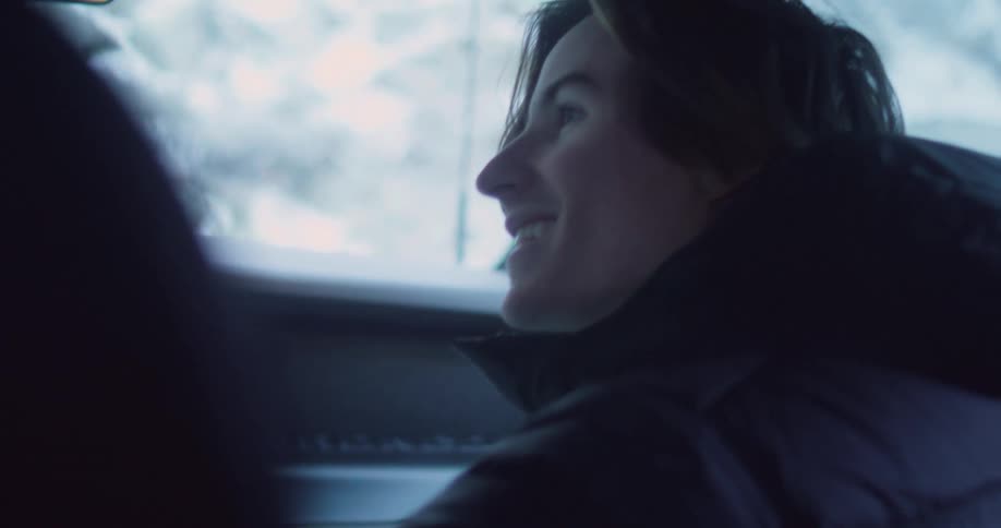 Man wearing a coat glances down then looks up and smiles at friends