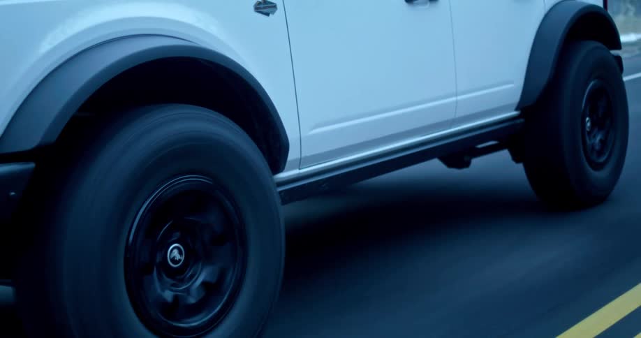 A white suv drives along a twolane road with snow lining the edges its black wheels in motion