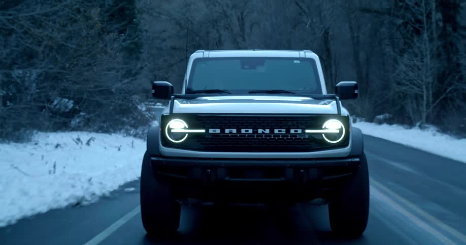 Bronco model vehicle drives past a snowy forest of leafless trees on a winter day