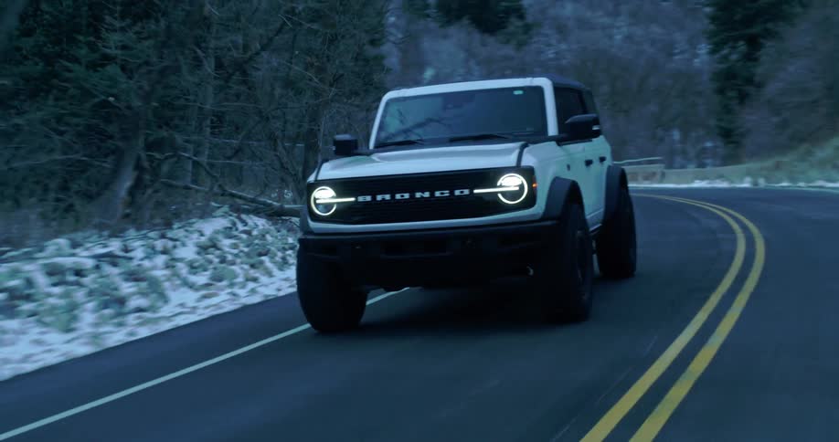 Ford bronco drives along a winding road in a winter region