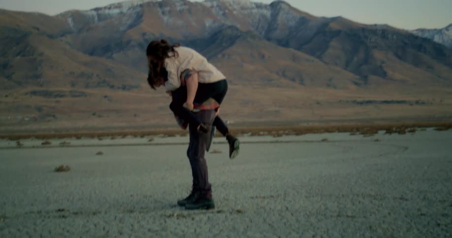 A young woman climbs onto a mans back as they have fun together in a badland at midday
