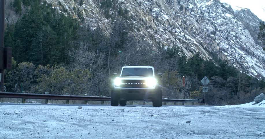 A snowy mountain road with a bronco suv driving through it on a winter day