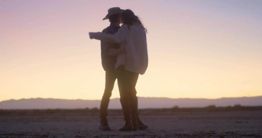 Couple dancing in the middle of a desert environment in the late afternoon