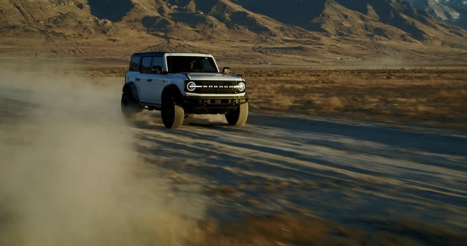 White ford bronco drives on a dirt road in the desert