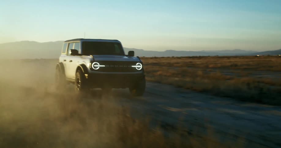 An suv drives along a dusty dirt road at sunset