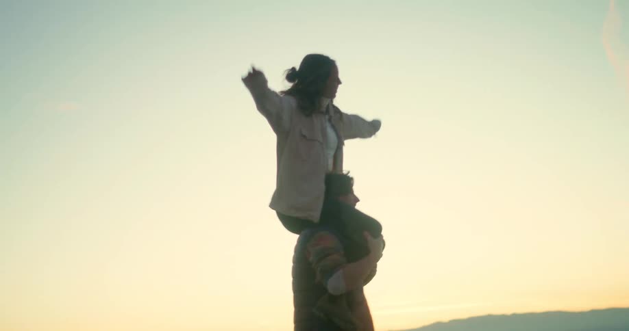 Cheerful woman sitting on the shoulders of a man who is walking in a desert environment