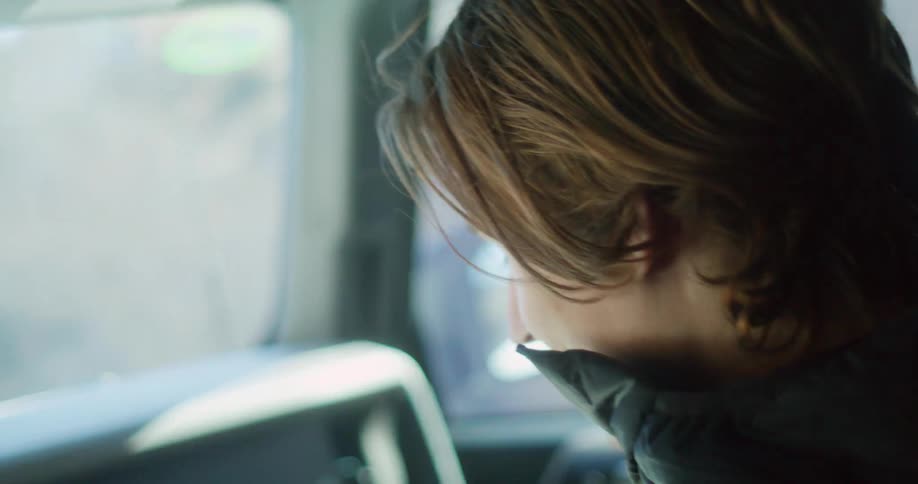 A man in a winter jacket sitting in the passenger seat of a car smiling as he talks to the driver and occasionally glances out the window