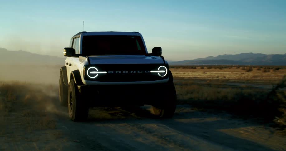 White ford bronco driving on a dirt road kicking up dust