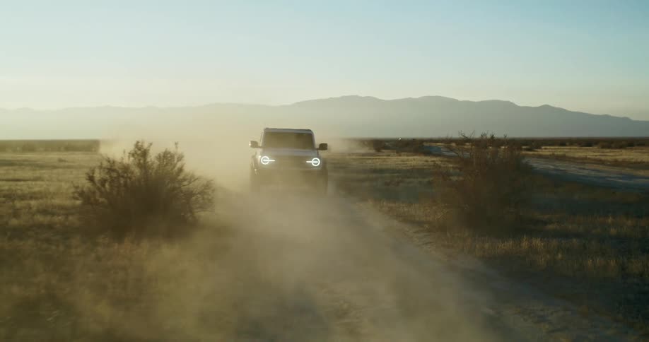 White suv driving on a dirt road kicking up dust at sunset
