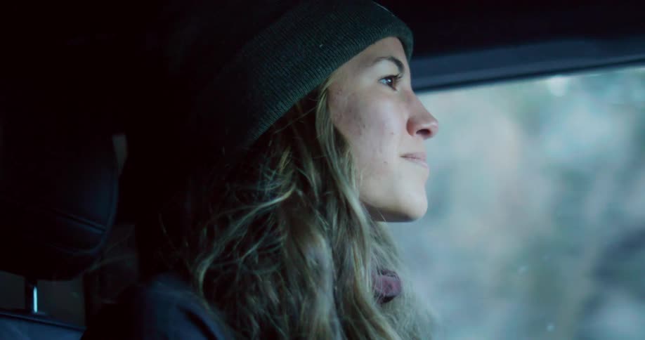 A woman wearing a beanie looks ahead intently with a smile while driving
