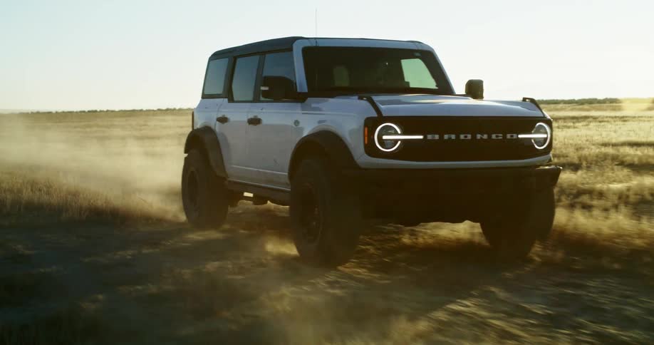 White ford bronco driving across a dry field kicking up dust
