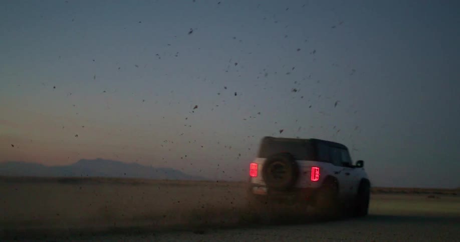 An offroad car driving in a desert environment releasing dust wherever it goes on a clear morning