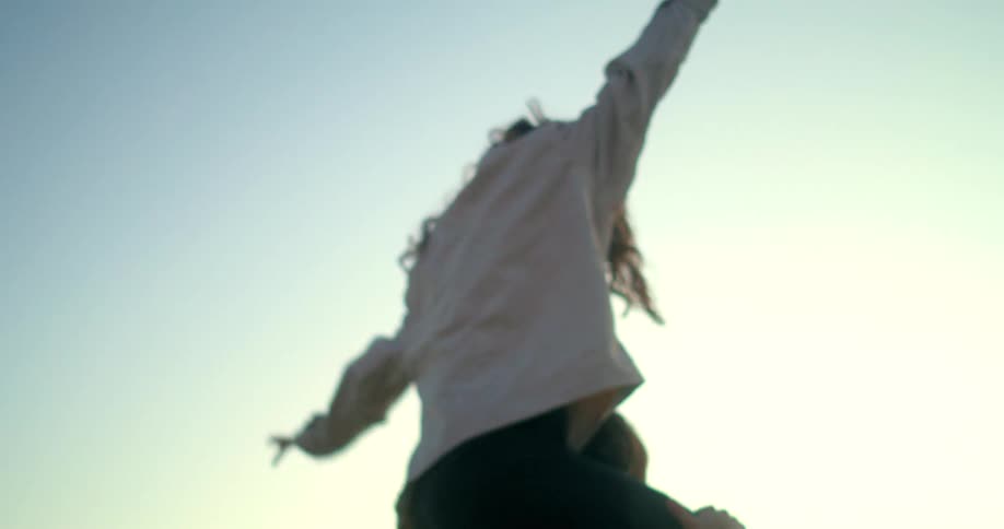 Woman smiles with open arms while sitting on a mans shoulders outdoors