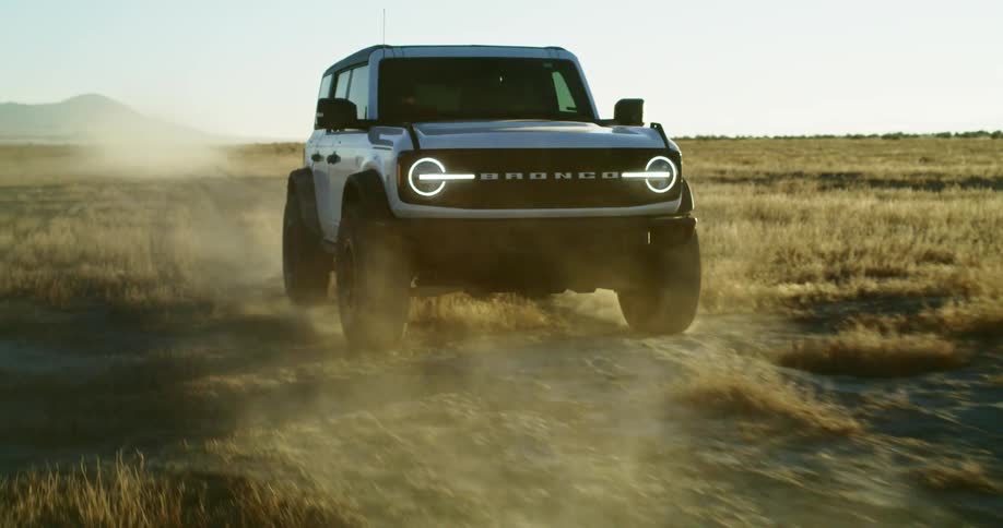 Ford bronco driving on a dirt road in the countryside during sunset