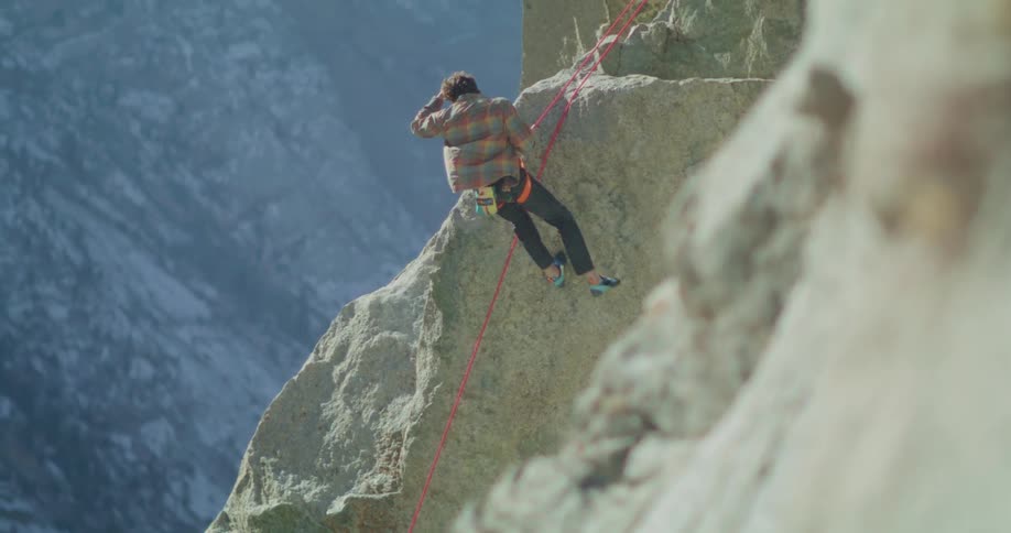 A man descending a rock using a pink rope that is attached to his waist