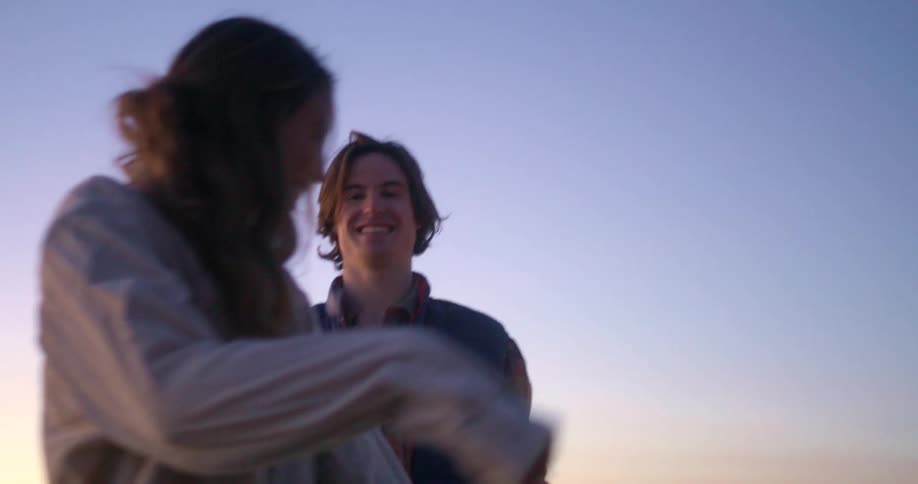 Two people smile at each other outdoors at dusk