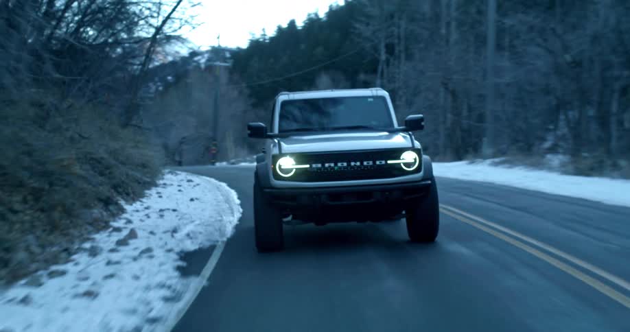 White ford bronco drives along a road surrounded by snow and bare trees