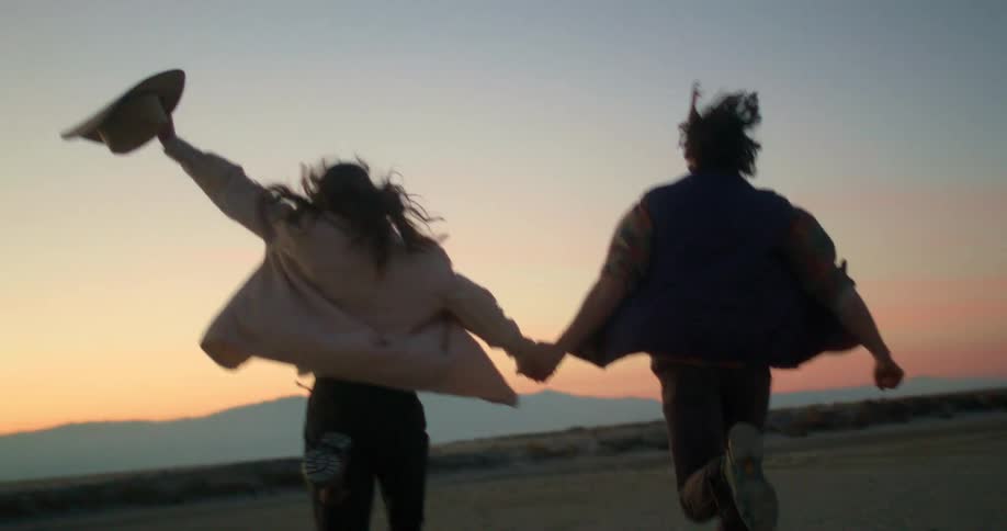 A young boy and girl run excitedly holding hands across a wide expanse of land at sunset