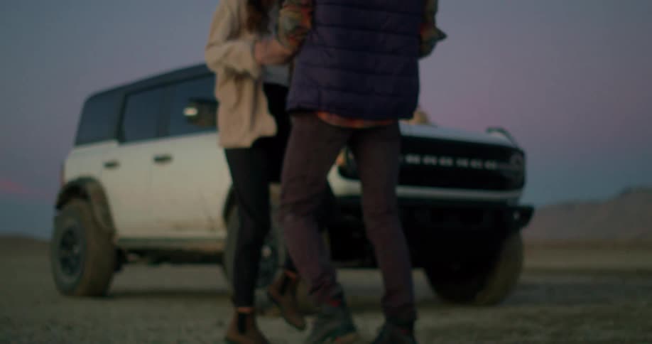 Couple dances in front of an offroad vehicle parked on arid ground