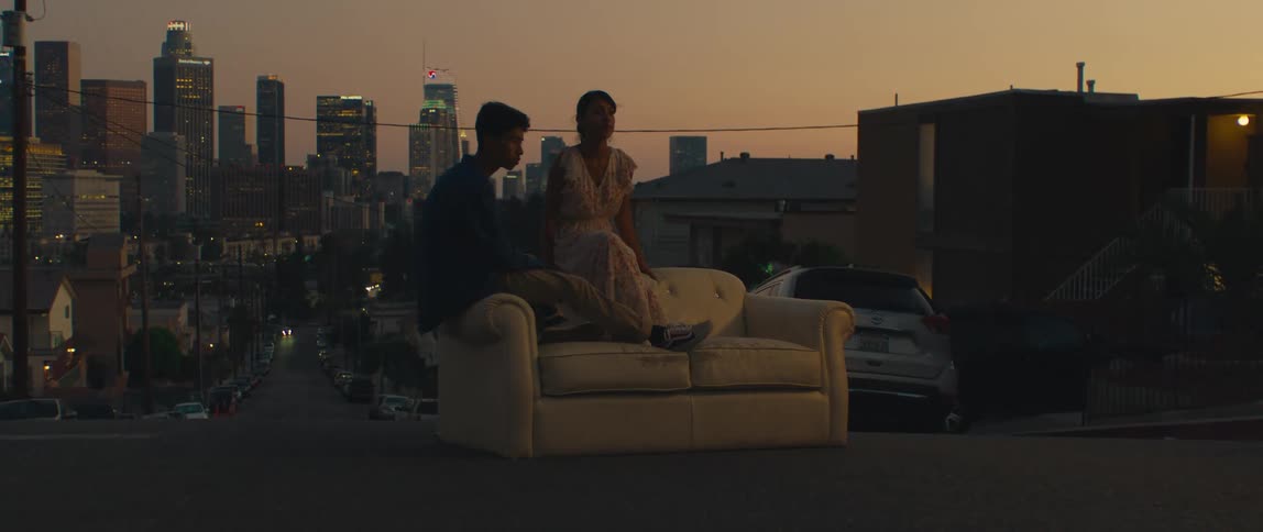 Couple sitting on a couch in the middle of the street with lit buildings in the background