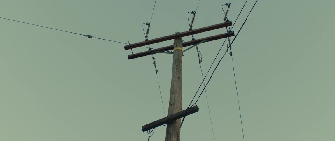 The video shows an angled lowangle shot of a utility pole with several telephone or power lines attached to it the pole is made of wood and the sky behind it is a dull overcast gray the watermark filmsupply is centered on the screen