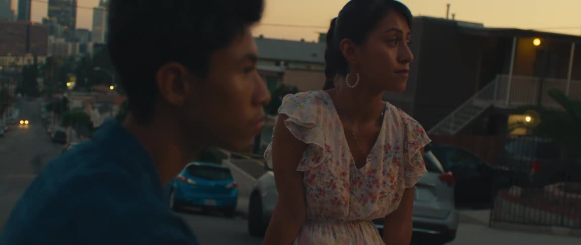 Two young people talk on a street at sunset with the city in the background
