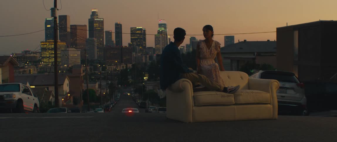 Couple sits on a couch in the middle of the street with the citys illuminated buildings in the background