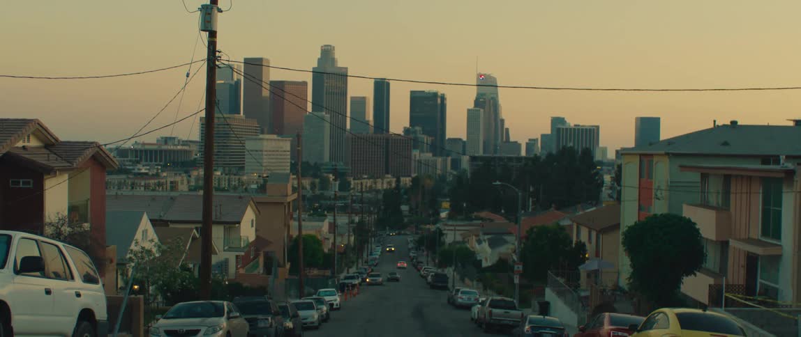 A suburban street view leads into a downtown city skyline at sunset