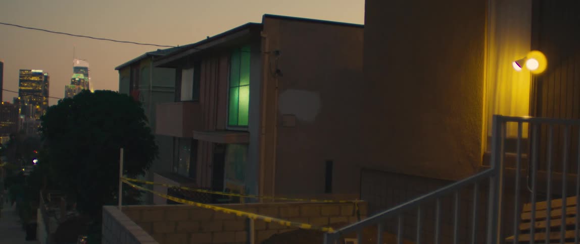 The video shows an exterior shot of a building at dusk there is a yellow caution tape across the bottom of the frame the building has multiple levels and a bright yellow light is visible from a porch or outdoor light fixture on the right side of the