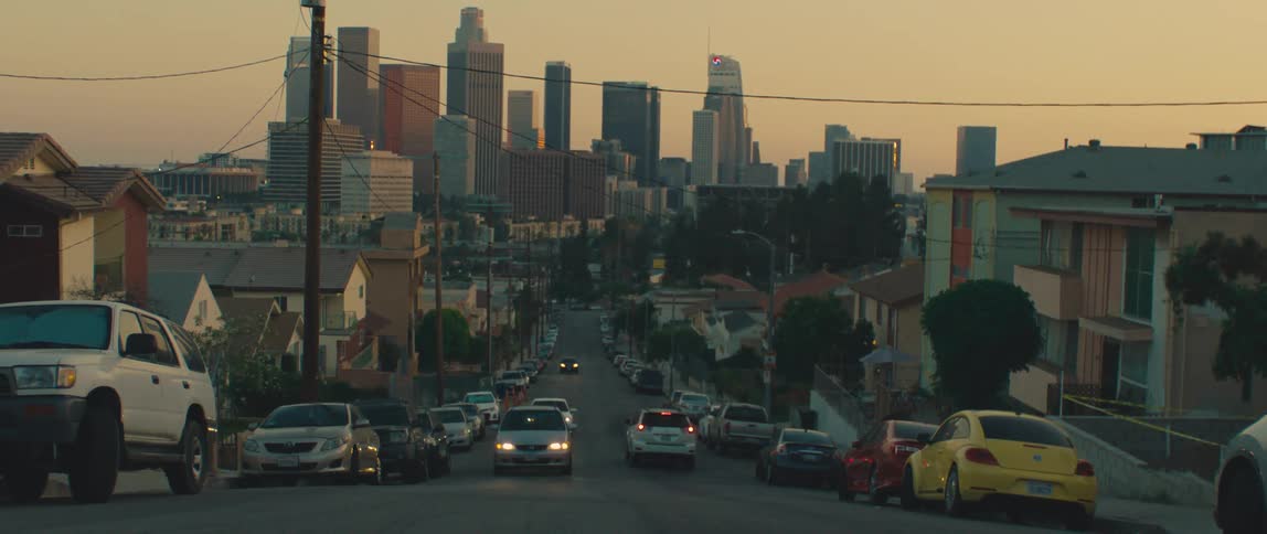 Urban road with parked cars in a suburb and skyscrapers of a metropolis on the horizon