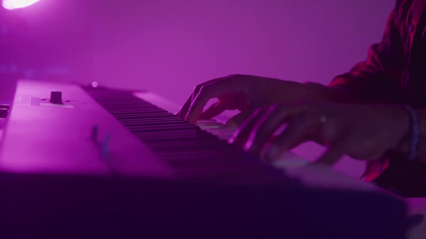 A persons hand playing on a piano in an indoor environment with pink lighting