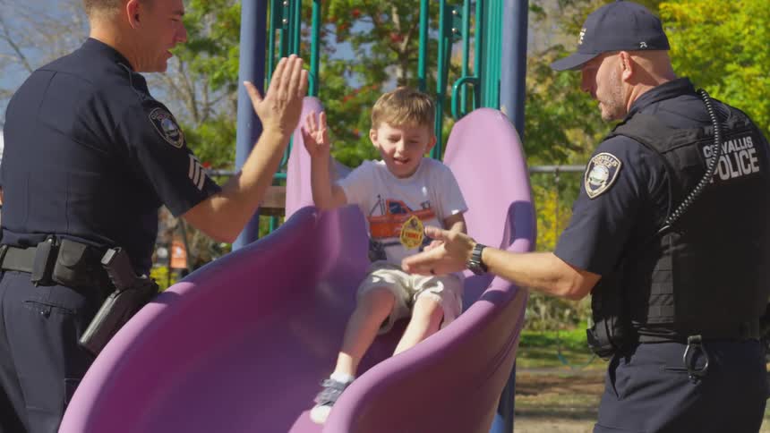 A boy slides down a playground slide and high fives police officers