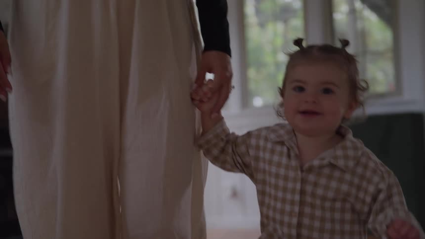 The face of a little girl who is walking indoors holding hands with an adult and smiling