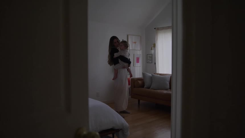 Woman holds a child in her arms inside a room lit by the window